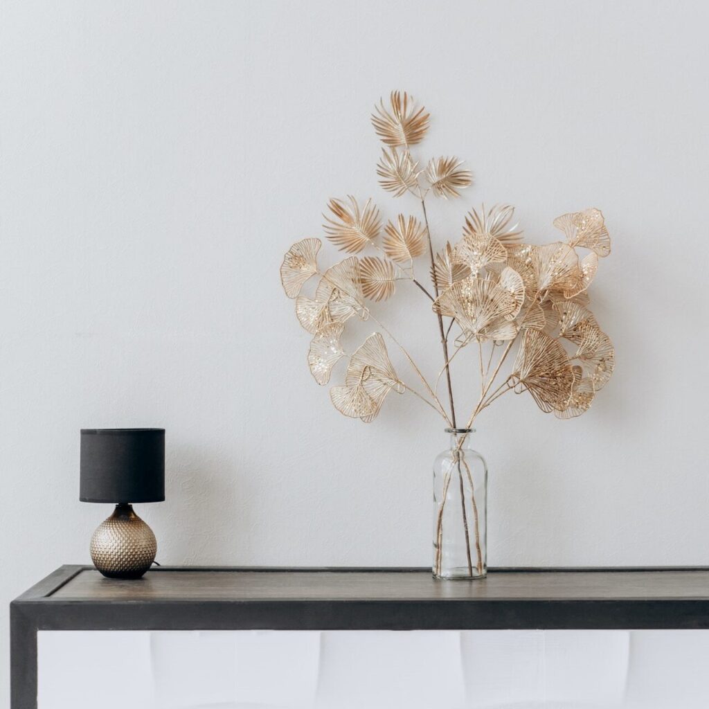 Flot minimalistisk rum med sort smalt bord og plante i guld, samt lille stort/guld lampe. 
