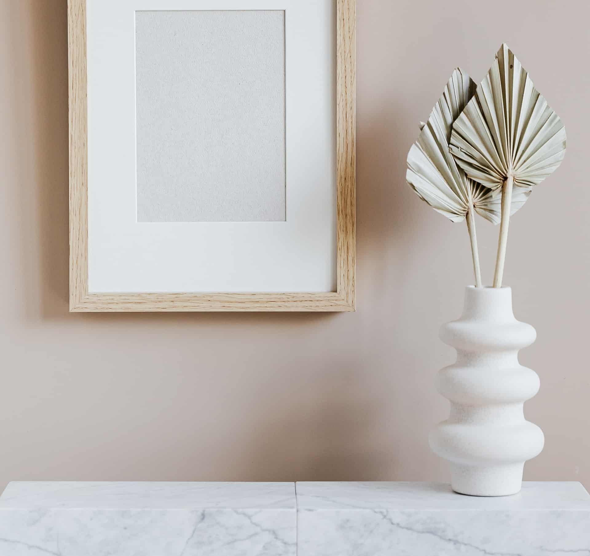 Nordisk indretning med fin hvid vase på marmor bordplade og billedramme i træ.