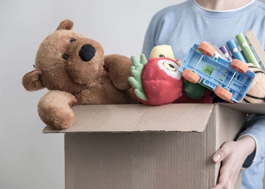 Barn bærer kasse med gammelt legetøj fra børneværelset som skal med og sælges på loppemarkedet. 