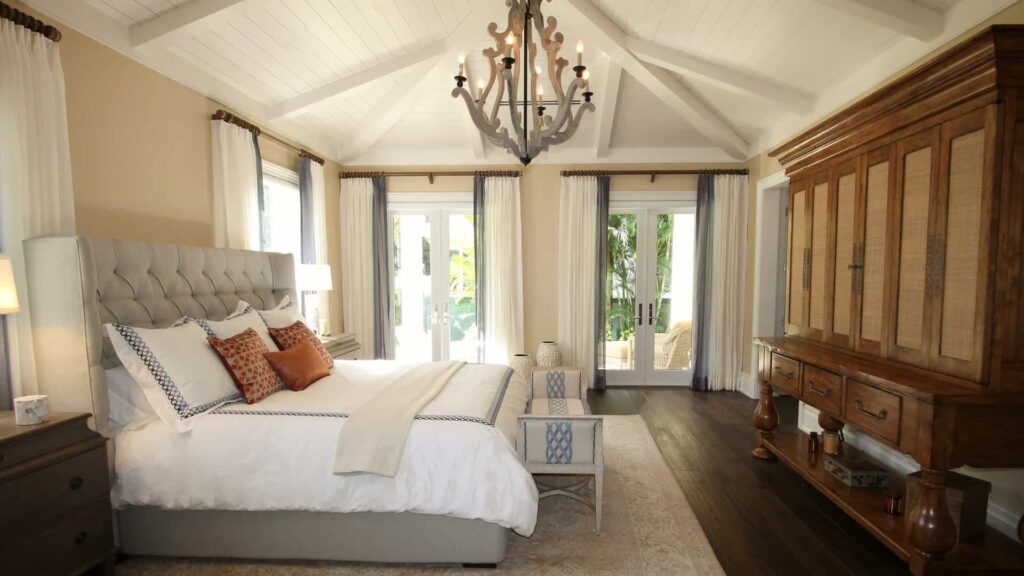 Smuk lysekrone i træmateriale over flot seng. Soveværelset er dekoreret i en elegant stil med træmaterialer, hvide og beige samt grå farver. 
